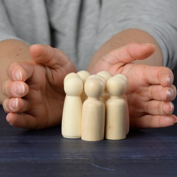 Female hands protect wooden figures of men. Protection and mentoring concept.